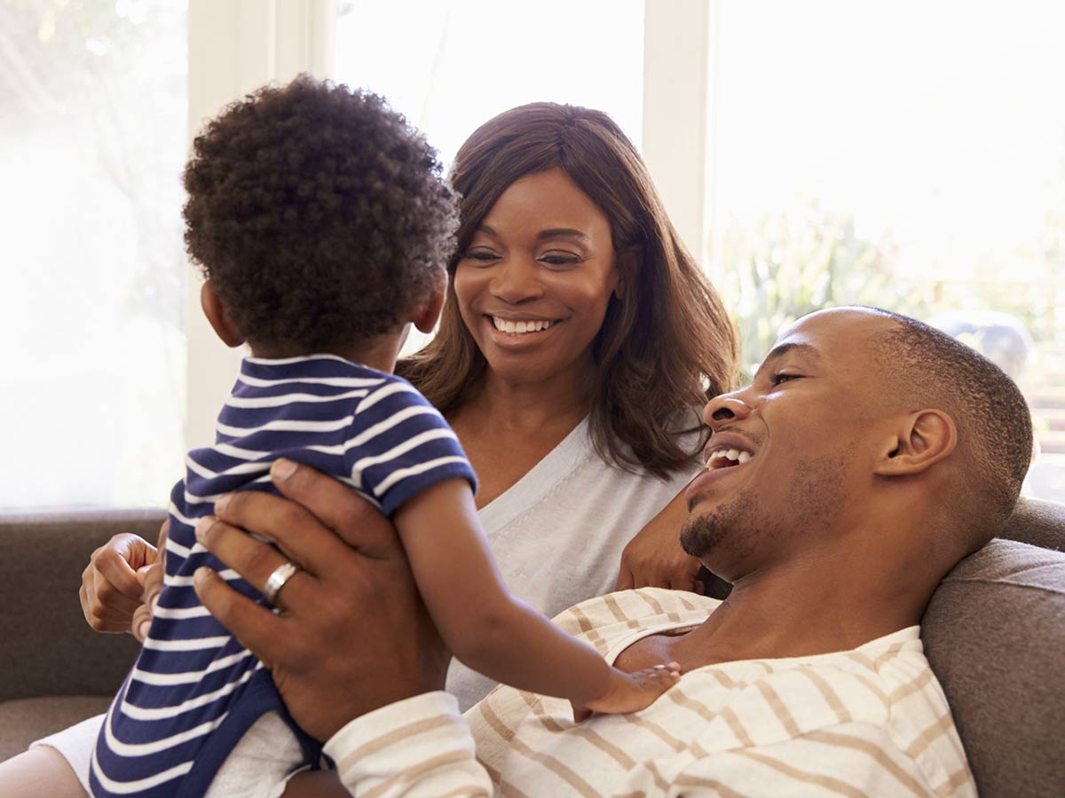 Mother and father sitting on their couch. Father is holding their small child.