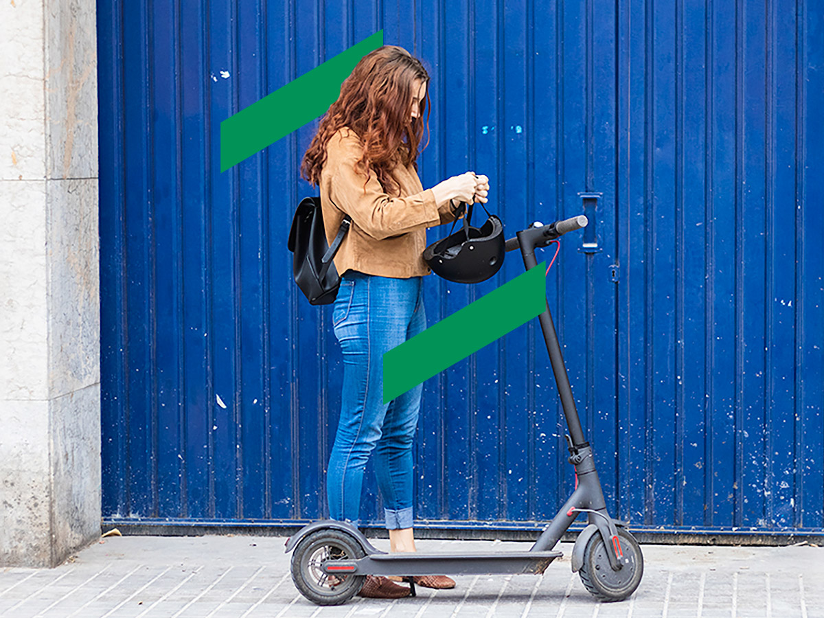 Mid-twenties male and female riding e-scooters side by side down a pedestrian roadway.